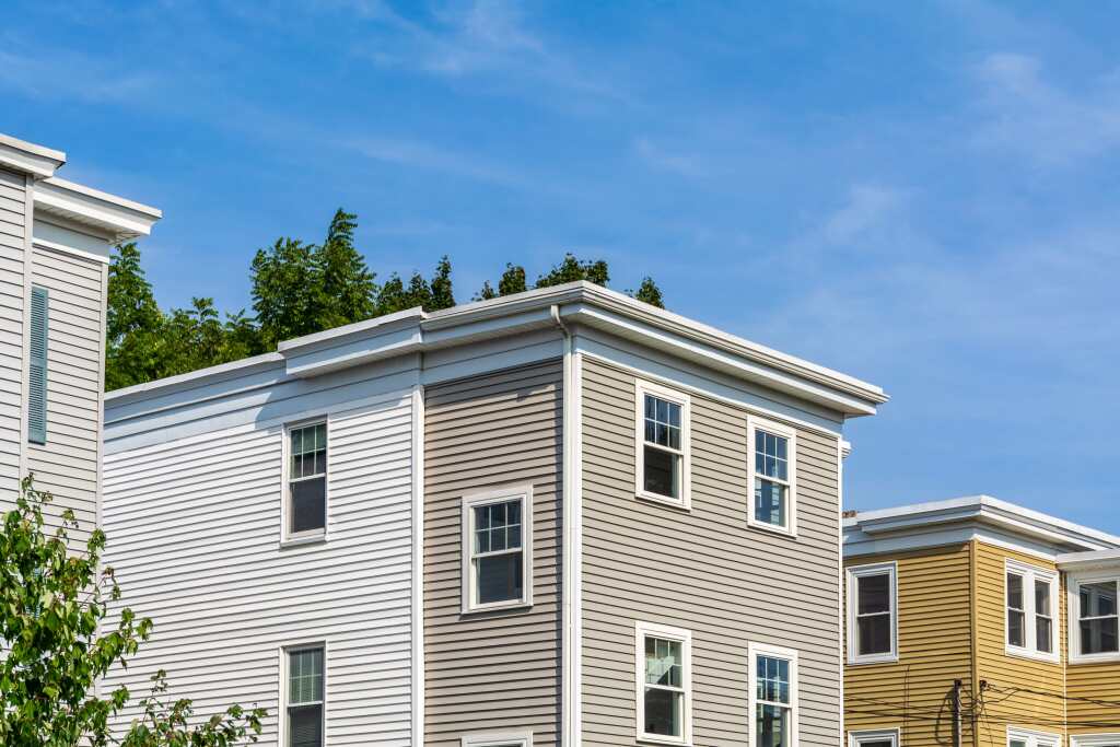 Modern residential buildings with gray and yellow vinyl siding under blue sky with white trim and multiple windows