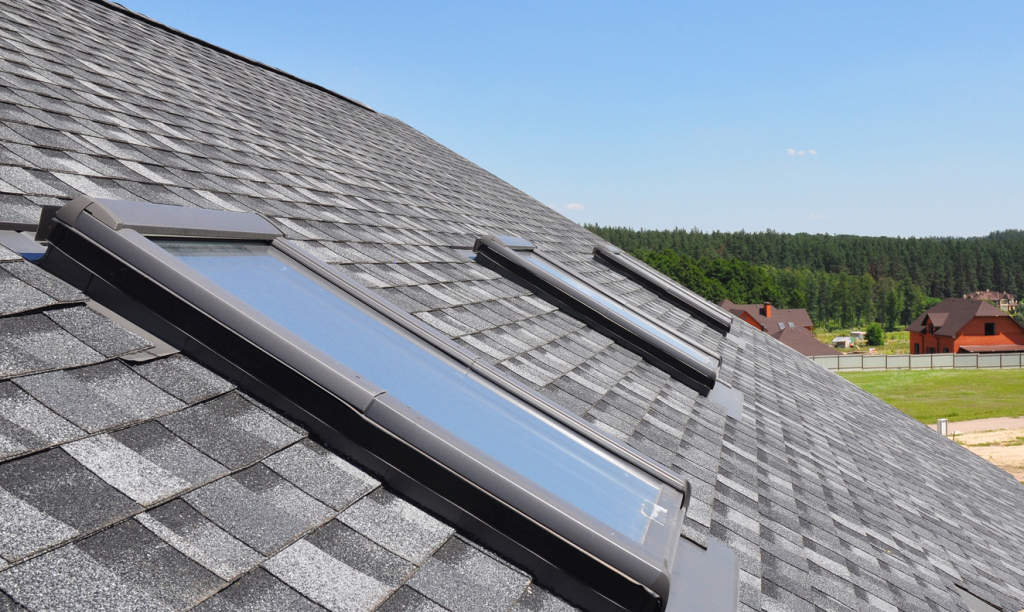 Modern roof skylights installed on gray asphalt shingle roof with forested hills and residential homes in background