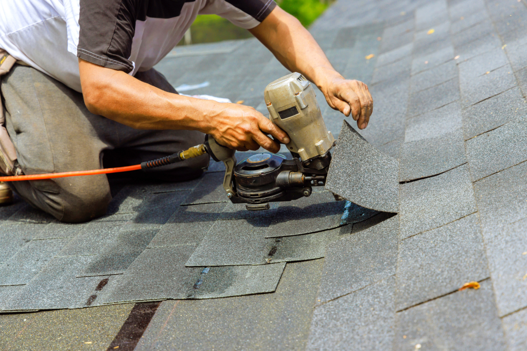 Construction worker using pneumatic nail gun to install asphalt shingles on roof during home renovation project