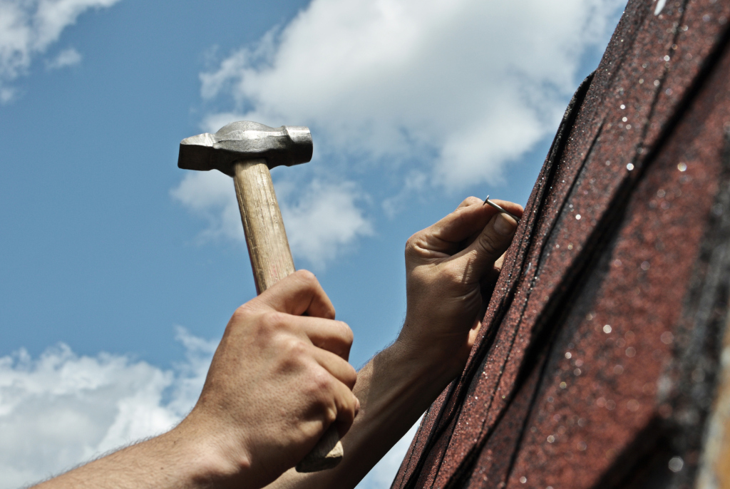 Person holding hammer while working on roof repair under blue cloudy sky, construction and home maintenance work