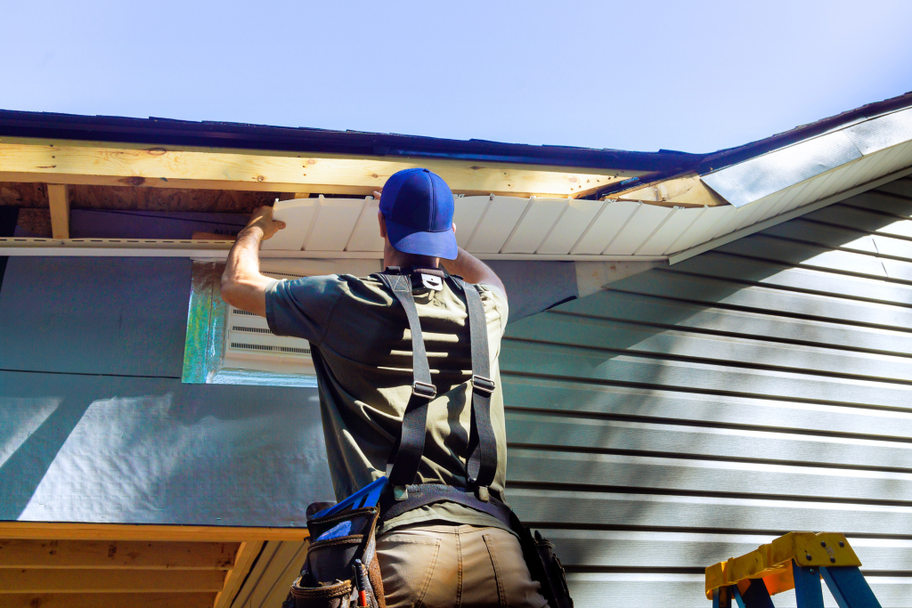 Construction worker in blue hard hat installing metal roofing panels on residential house with safety harness