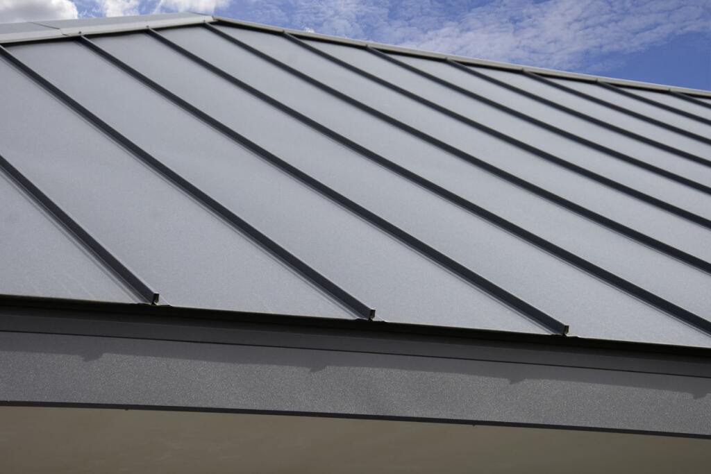Gray metal roof with standing seam panels and raised ribs against blue cloudy sky, showing modern residential roofing material