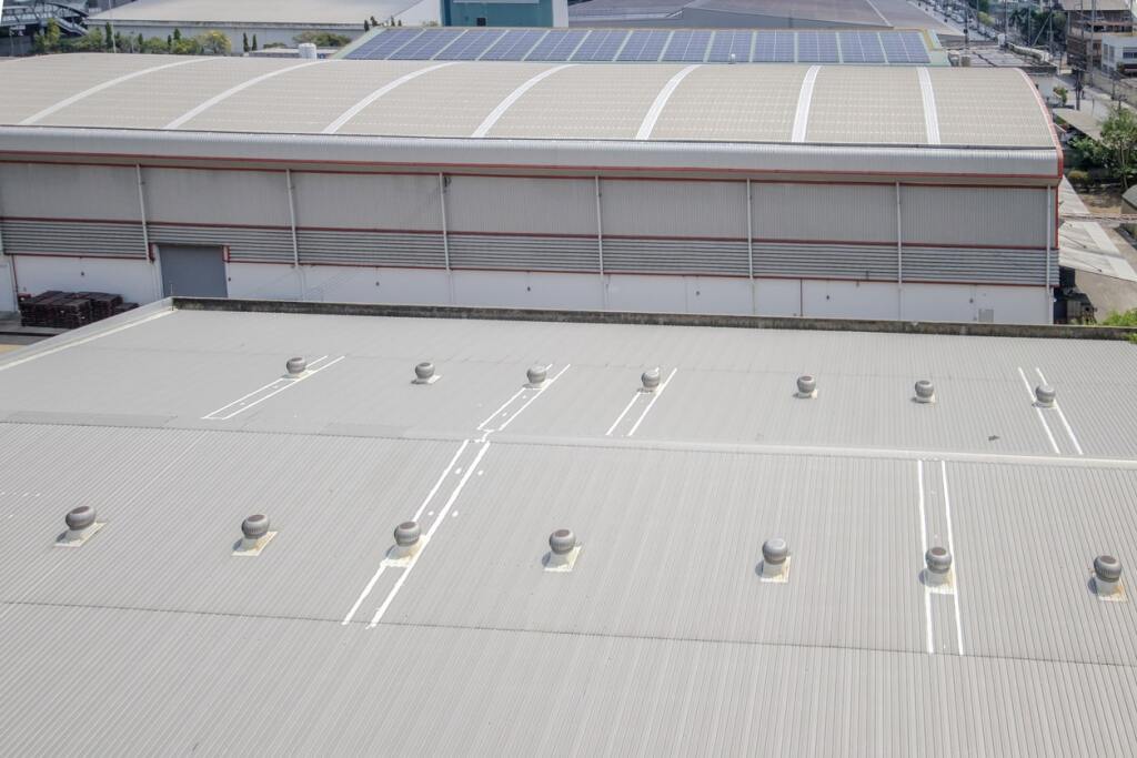 Aerial view of industrial warehouse building with metal roofing, solar panels, and ventilation systems in commercial area
